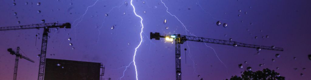 A lightning bolt strikes near cranes on a building site during a night storm