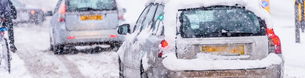 Cars and a cyclist moving on a busy road in snowy conditions