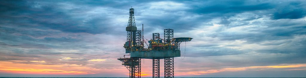 An offshore oil rig in blue choppy waters with a blue cloudy sky in the background