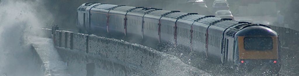 Intercity train in Dawlish moving along a coastal bridge with waves crashing over it.