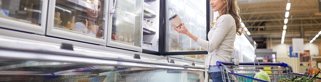 A woman picking up a tub of ice cream in the frozen aisle of a supermarket