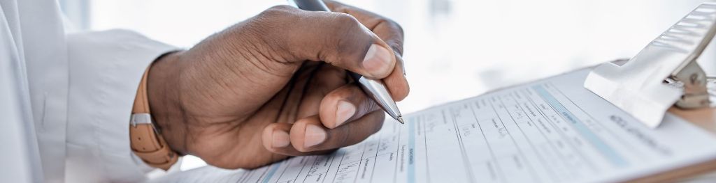 A pair of hands holding a clipboard with a document. The left hand holds a black pen.