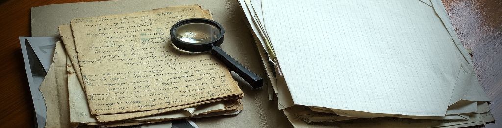 Old, yellowed papers marked with cursive handwriting, with a magnifying glass resting on the top.