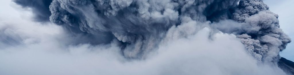 A volcanic eruption with ash cloud, viewed from the ground through clouds