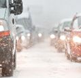 A view between two rows of traffic with headlights on, in the snow.