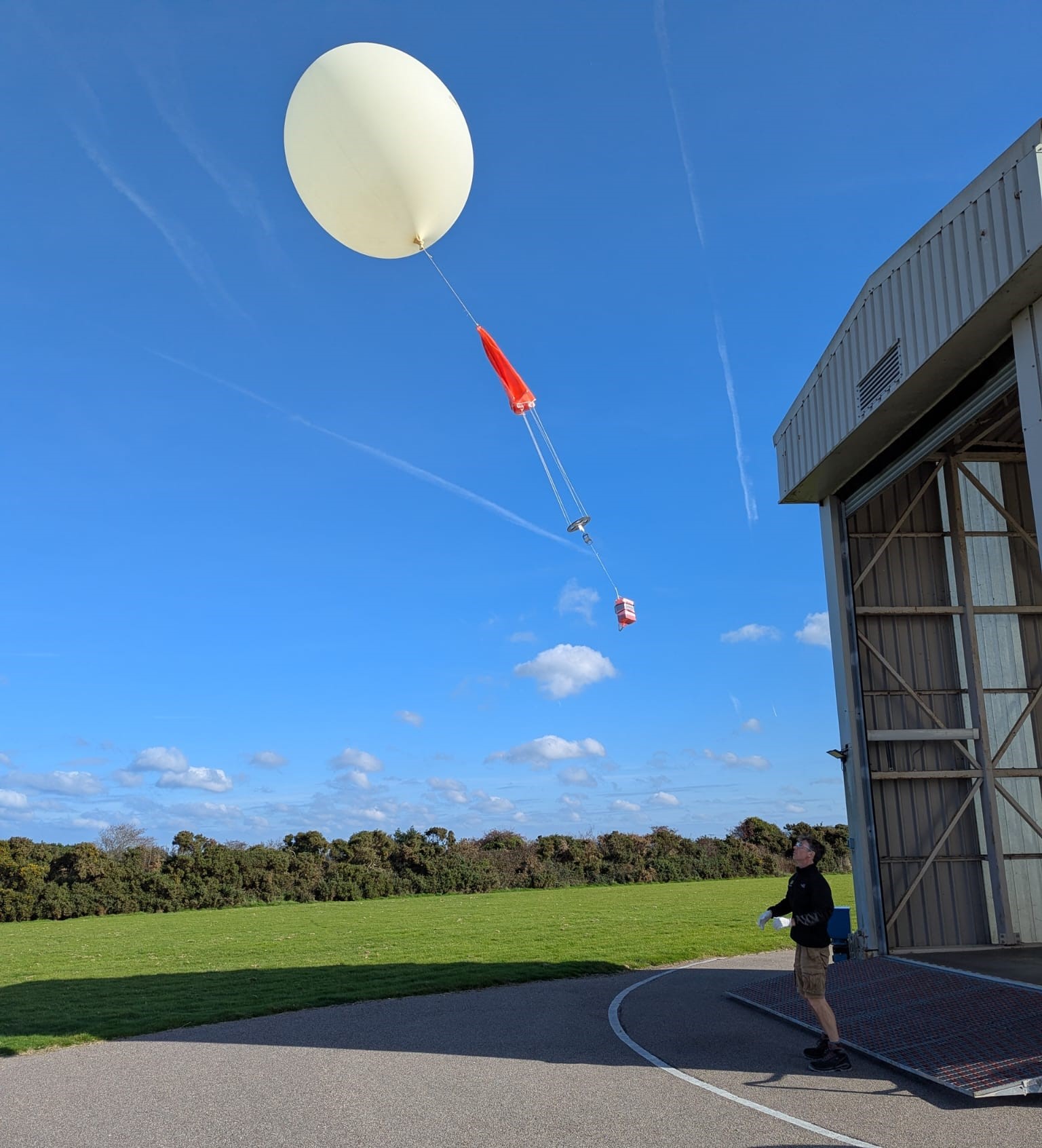 The image shows a technician in front of a warehouse releasing a weather balloon into the sky