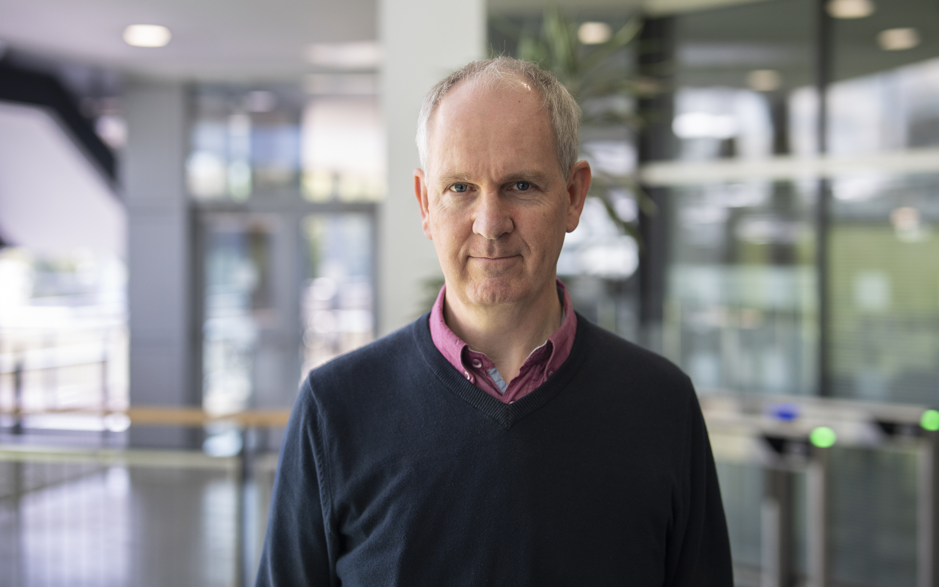 Rowan Sutton in a blue jumper and red shirt standing for a portrait photo in Met Office HQ.