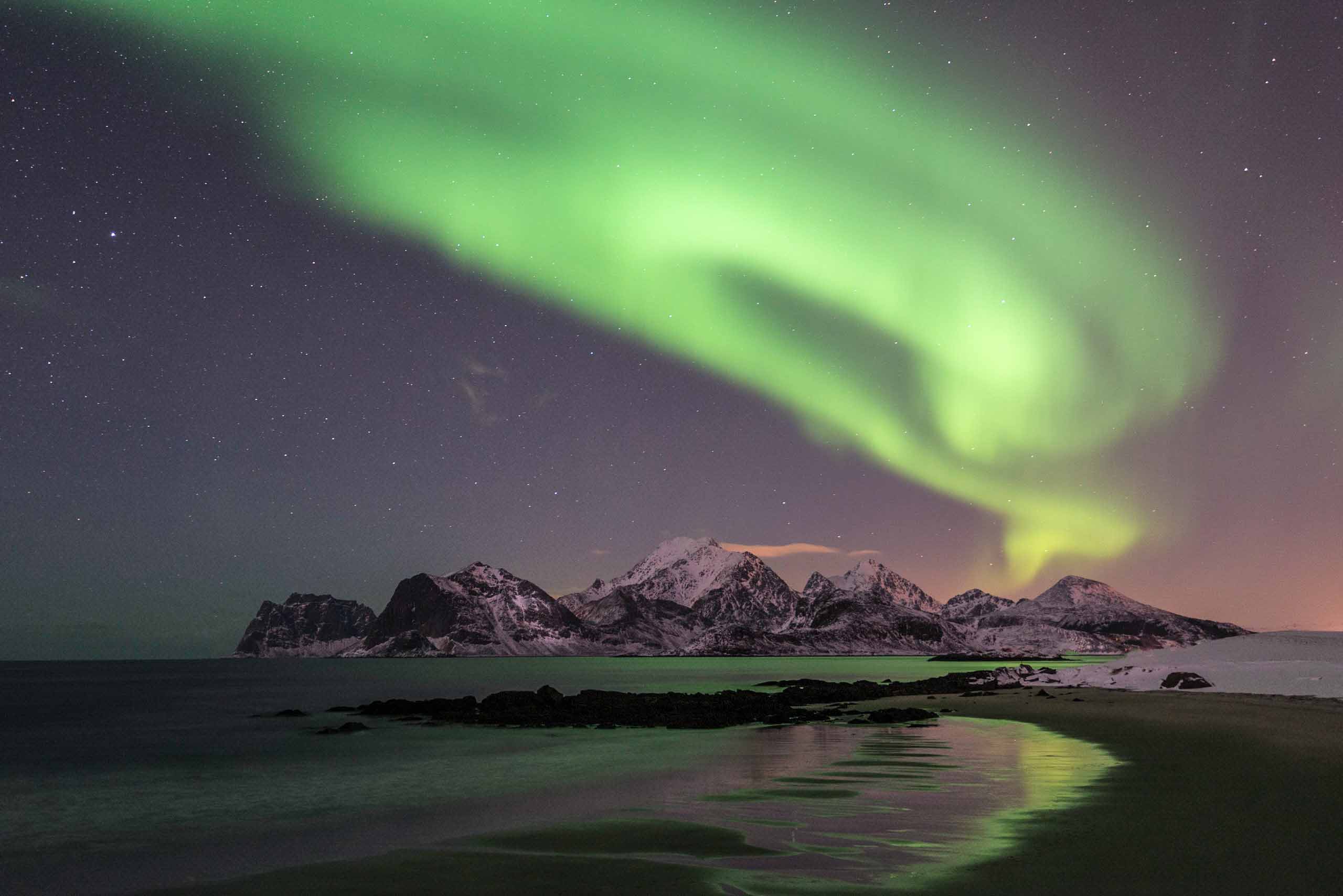 Aurora Borealis in the night sky over mountains and a dark beach.